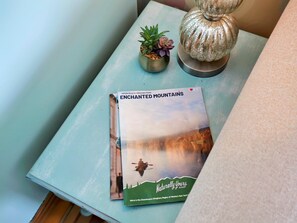 A table with a book titled 'ENCHANTED MOUNTAINS' and a decorative lamp.