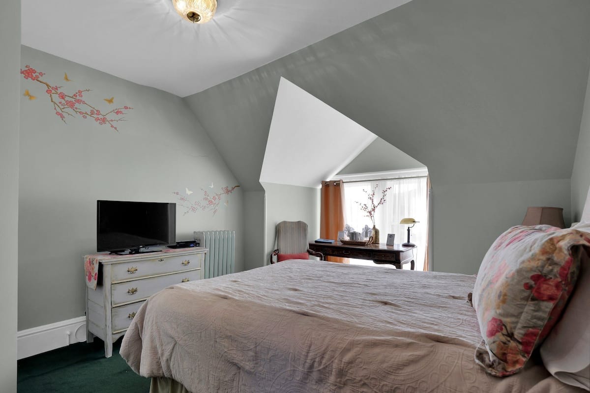 A bedroom with a large bed, a dresser, a television, and a desk with a lamp.