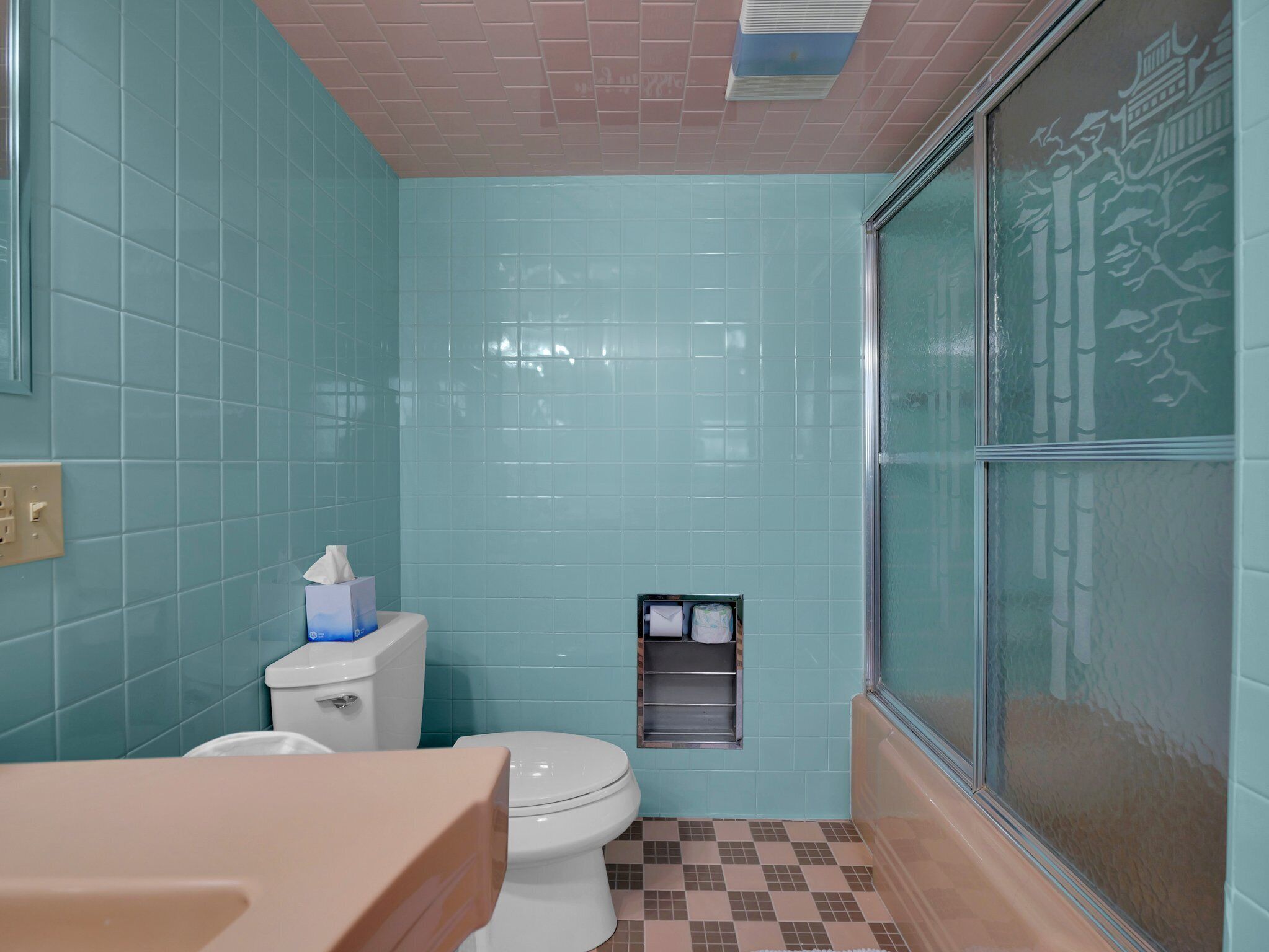 A bathroom with teal tiles, a white toilet, a sink, and a shower area with a glass door.