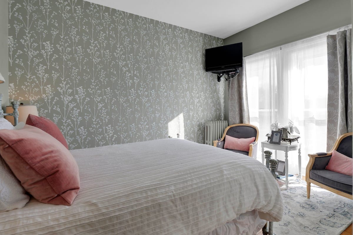 A bedroom with a bed, two chairs, a small table, and a TV.