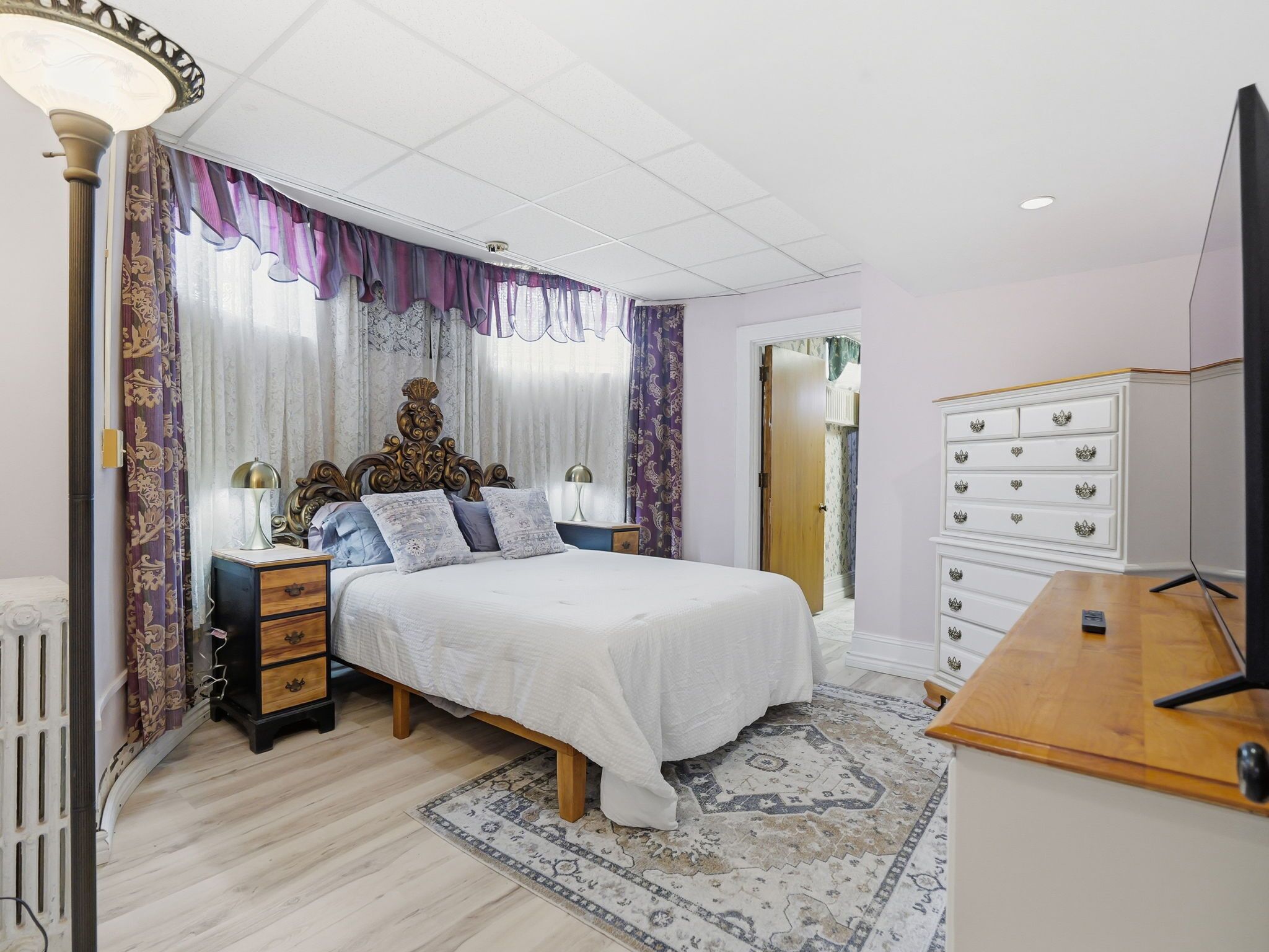 A bedroom with a large bed, wooden nightstands, a dresser, and a television.