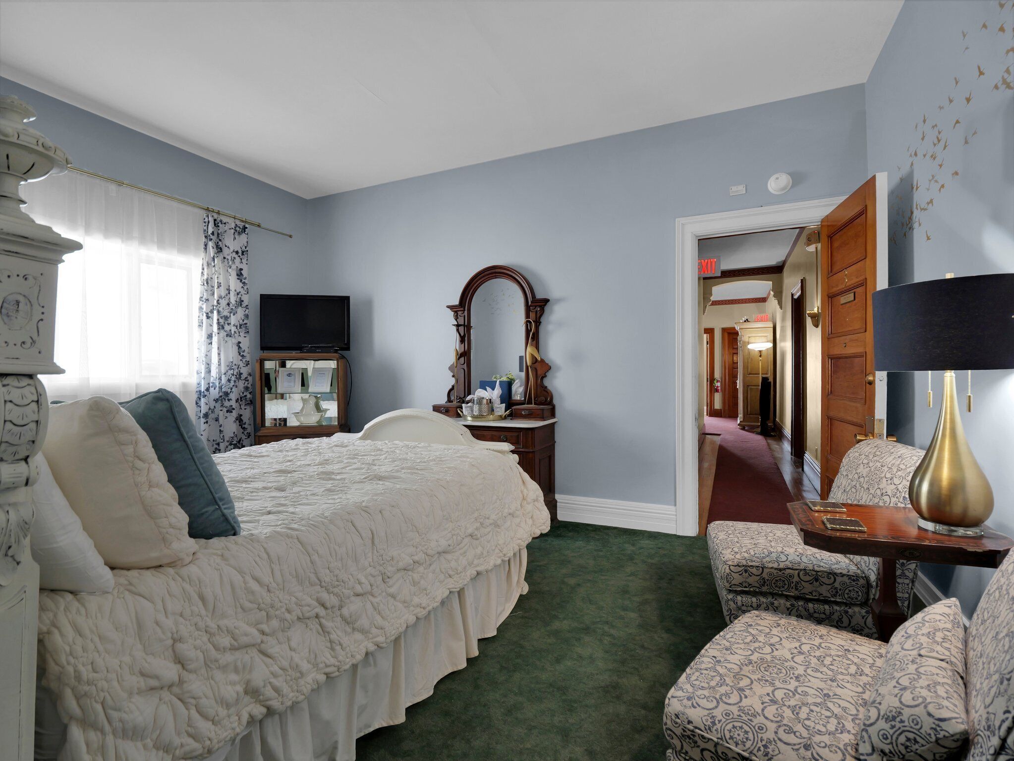 A bedroom with a large bed, a dresser, a mirror, a television, and a chair.