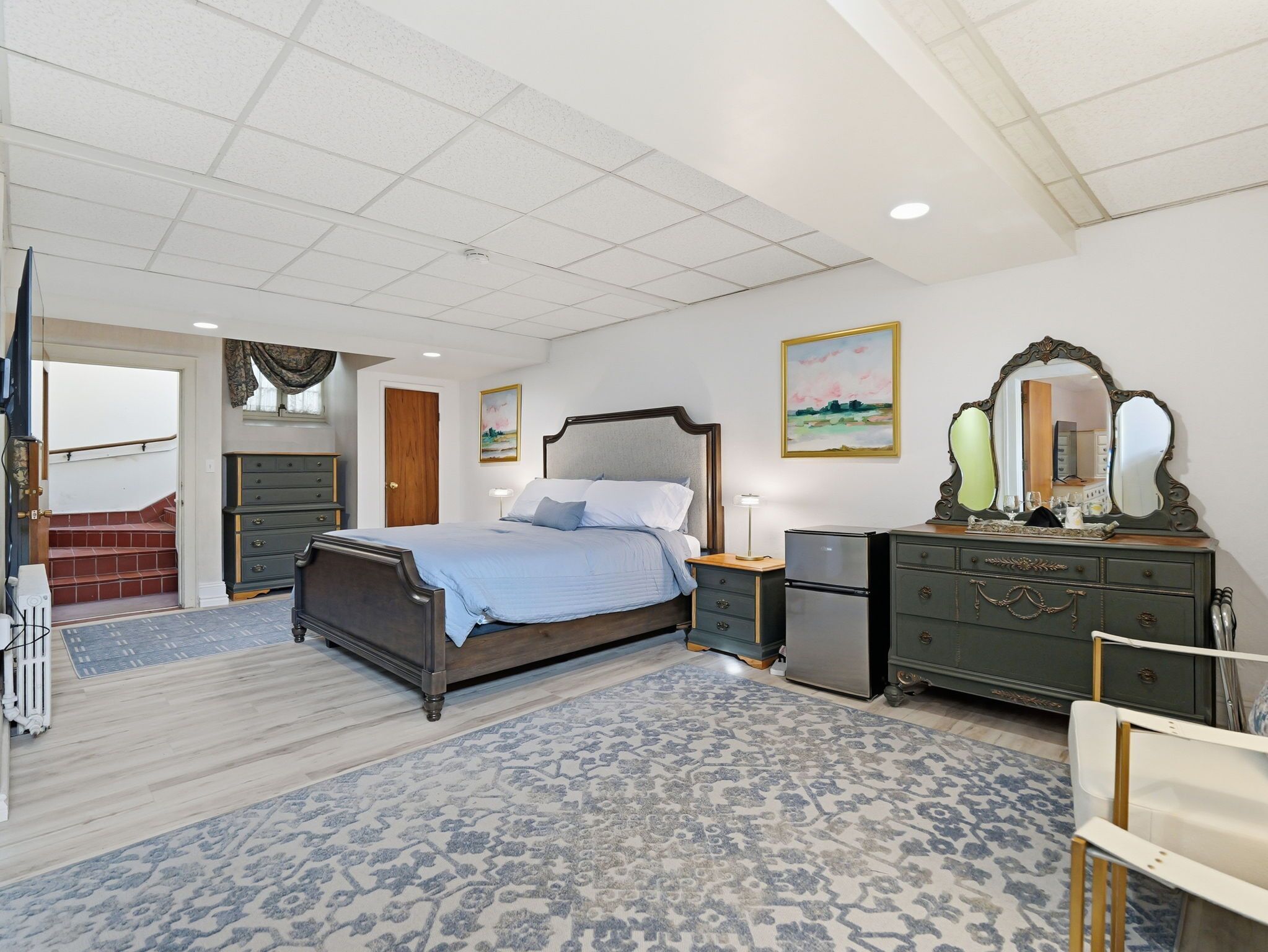 Een slaapkamer met een bed, een dressoir, een nachtkastje en een spiegel.