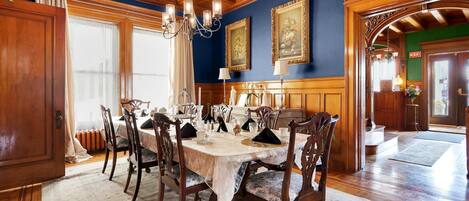 Uma sala de jantar formal com teto de madeira, um candelabro e uma mesa posta para seis pessoas.