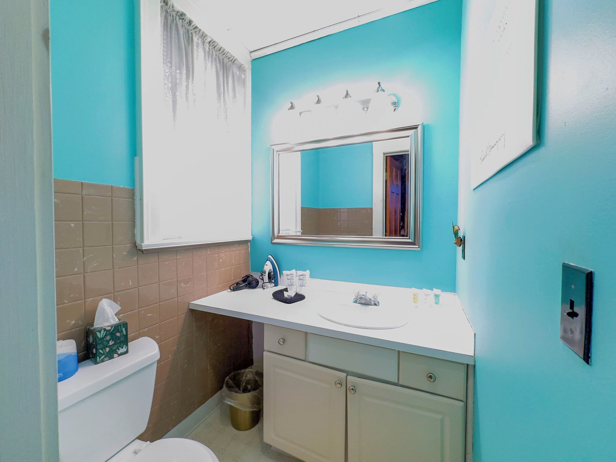 A bathroom with a white toilet, a sink with toiletries, a mirror, and a trash bin.