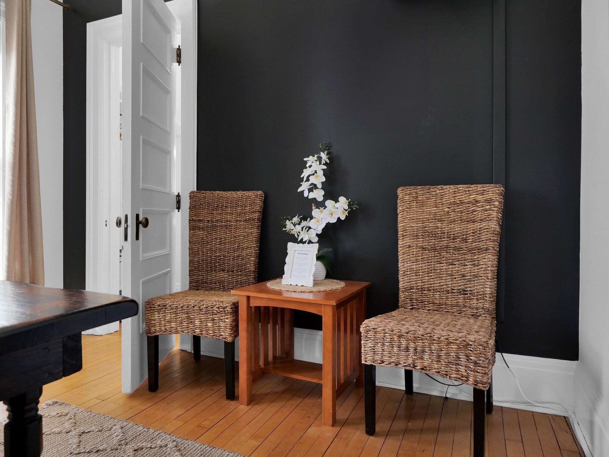 A room with two wicker chairs, a small wooden table, and a vase with white flowers.