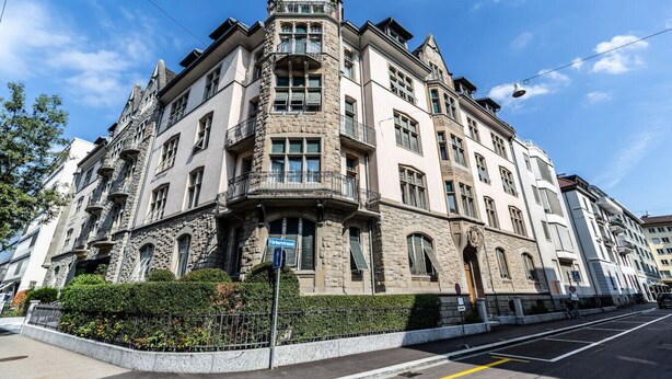 En historisk bygning med et hjørnetårn, en facade i sten og mange vinduer.