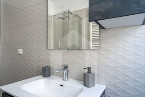 Une salle de bain avec un lavabo blanc, un miroir et un espace douche.