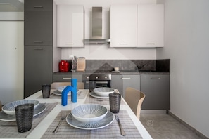 Une cuisine moderne avec des meubles gris, une hotte en acier inoxydable et une table à manger dressée avec des assiettes et des verres.