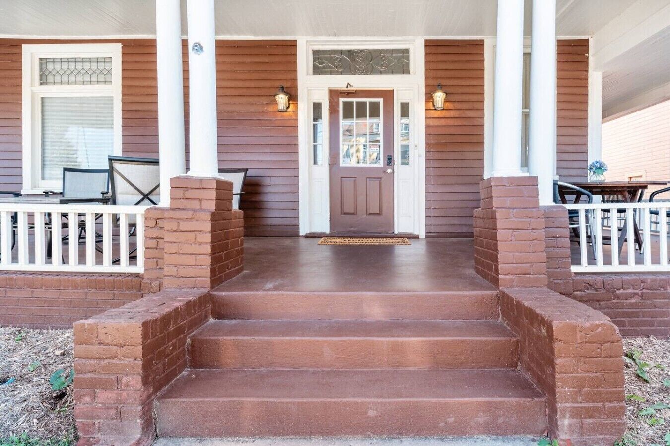 Une véranda à l’avant de la maison, avec un escalier menant à une porte, un banc et une table.
