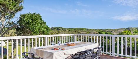 An outdoor dining area with a table set for two, surrounded by a white railing, overlooking a scenic landscape.