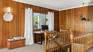 Una habitación con paneles de madera, un escritorio con computadora, una escalera y vistas al exterior con vegetación.