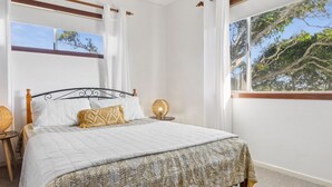 Un dormitorio con una cama, una mesita de noche con lámpara y una ventana con vistas a árboles.