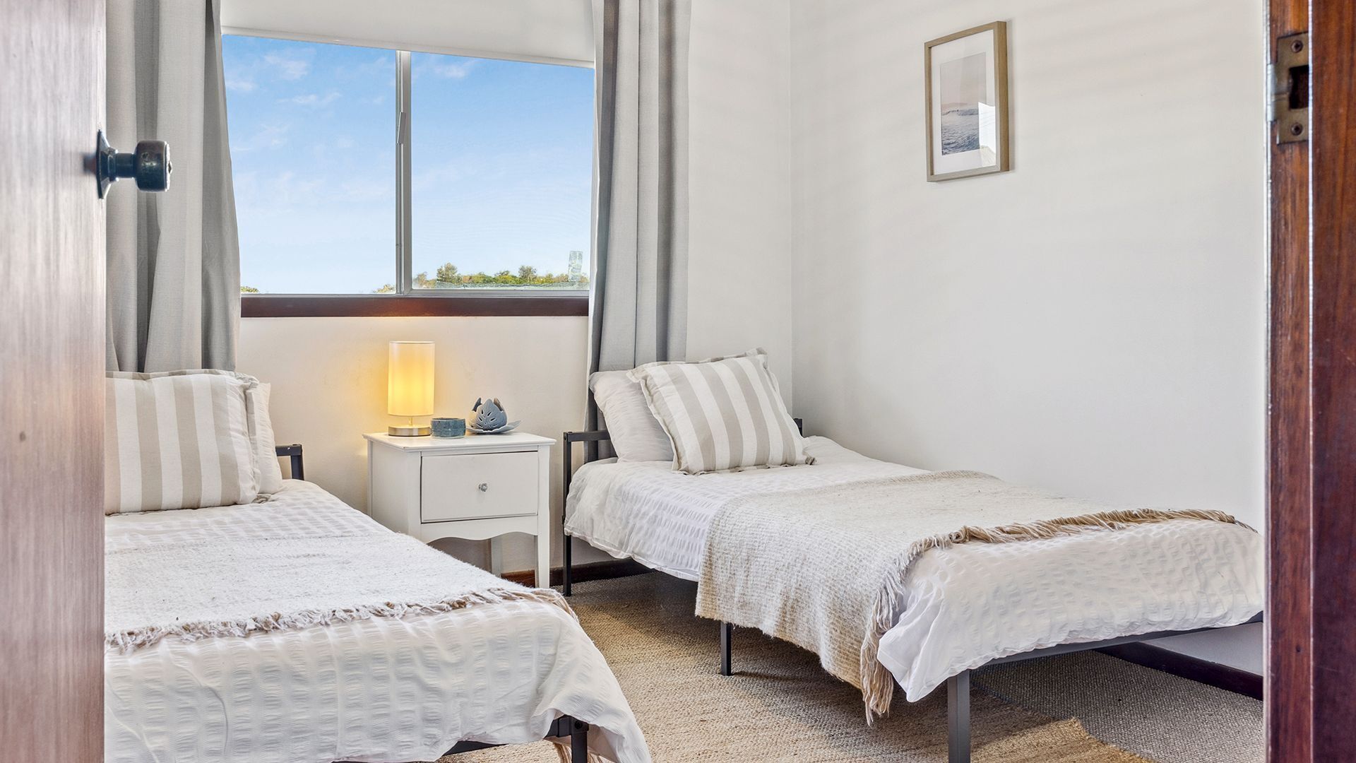 A bedroom with two beds, a nightstand with a lamp, and a framed picture on the wall.