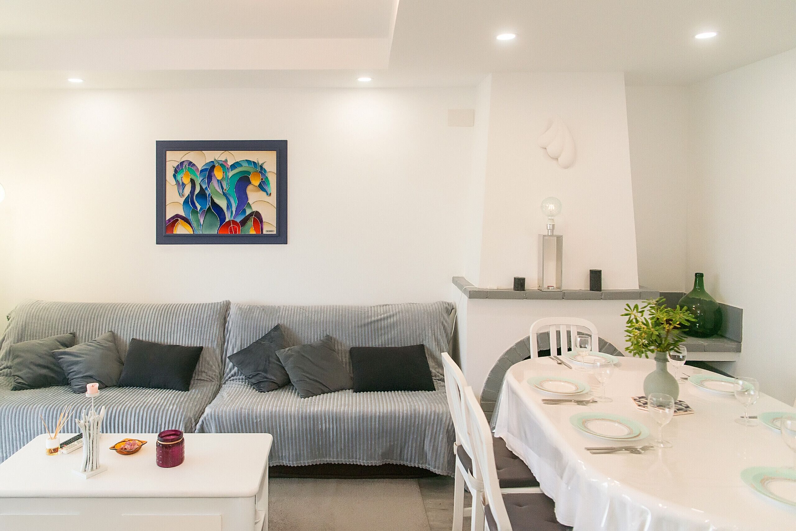 A living room with a striped sofa, a dining table set for two, and a colorful abstract painting on the wall.