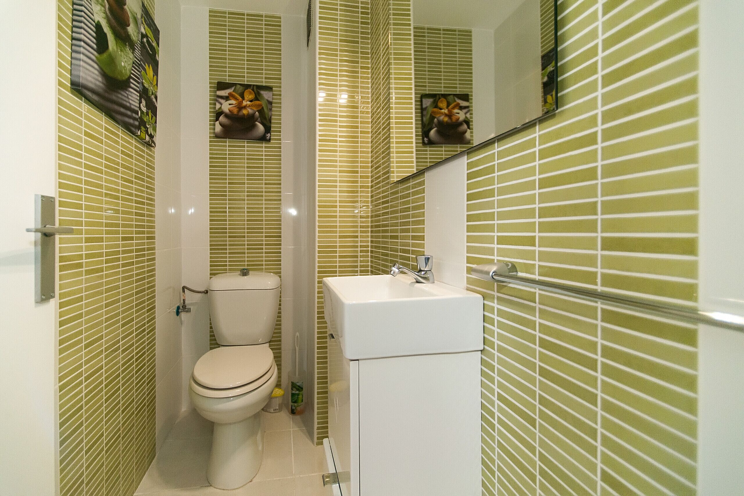 A bathroom with green-striped tiles, a white toilet, and a white sink with a mirror above it.