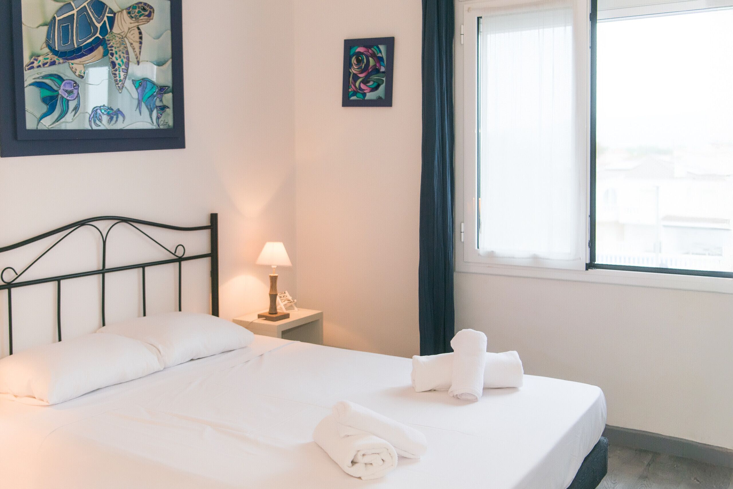 A neatly made bed with white linens and towels, a bedside lamp, and artwork on the walls.