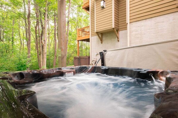 A hot tub with a wooden deck and a view of a forested area.