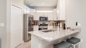 A modern kitchen with white cabinetry, stainless steel appliances, a granite countertop, and two bar stools. - Dream Condo Lakewood Ranch with Pools & On Site Restaurant (Bradenton)