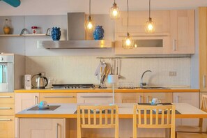 Una cocina moderna con armarios de madera, una campana extractora de acero inoxidable, una cafetera y lámparas colgantes.
