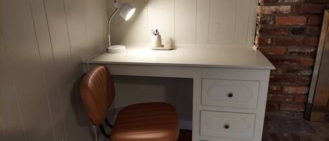 A compact workspace with a white desk, a brown leather chair, a desk lamp, and a small basket on a shelf.