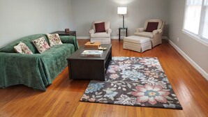 Ein Wohnzimmer mit einem grünen Sofa, zwei Sesseln, einem Couchtisch und einem floralen Teppich.