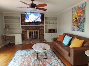 Cozy living room with a brick fireplace, leather sofa, and vibrant artwork.