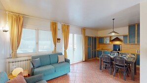 A compact living space with a sofa, dining table, chairs, and a kitchenette. - Appartamento Gloria by Bookinggardalake (Manerba del Garda)