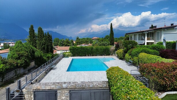 A rectangular swimming pool with a stone deck, surrounded by lush greenery and a stone wall. - Appartamento Gloria by Bookinggardalake (Manerba del Garda)