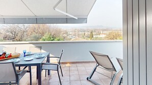 A balcony with a table set for two, a chair, and a view of a residential area. - Appartamento Gloria by Bookinggardalake (Manerba del Garda)