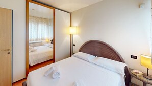 A hotel room with a bed, a bedside lamp, a mirror, and a door. - Appartamento Gloria by Bookinggardalake (Manerba del Garda)