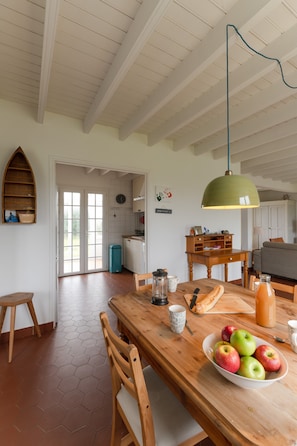 Une cuisine spacieuse avec une table en bois, un saladier rempli de pommes et un luminaire vert suspendu.