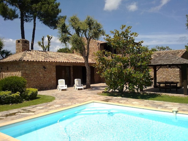 Relax by the serene pool surrounded by lush greenery and rustic stone buildings.