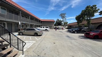 Ein Parkplatz mit mehreren Autos, ein Gebäude mit rotem Ziegeldach und eine Treppe, die zu einem Hauseingang führt.