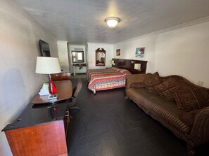 A hotel room with a bed, a sofa, a desk with a lamp, a mirror, and a ceiling light. - Vista Motel - Riverside (Riverside)