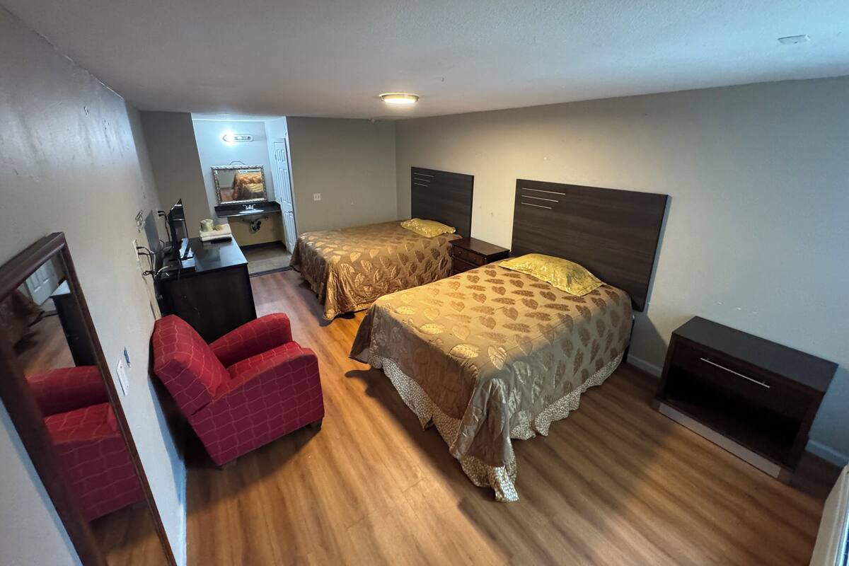 A compact hotel room with two single beds, a small desk, a chair, and a wardrobe.