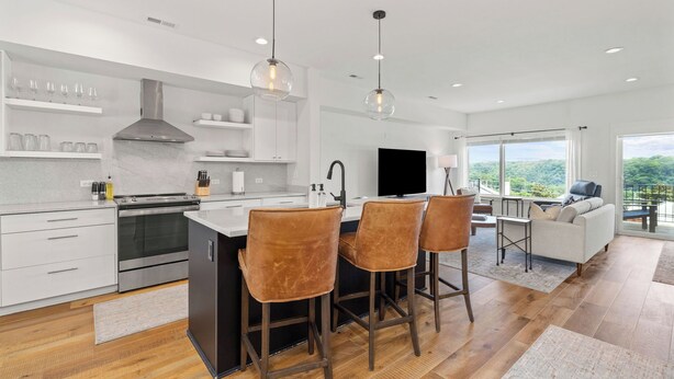 A modern kitchen with a central island, bar stools, and a dining area with a sofa and table.