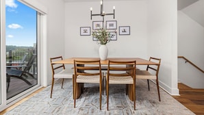 A dining area with a wooden table, four chairs, a vase with flowers, and framed pictures on the wall.
