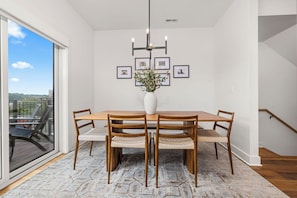Un comedor con una mesa de madera, cuatro sillas, un jarrón con flores y cuadros en la pared.
