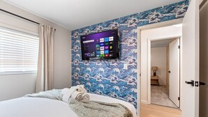 Quarto de hotel com cama, televisão montada exibindo interface de serviço de streaming e papel de parede em estilo tradicional japonês.
