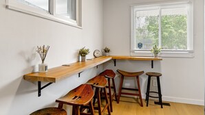 Uma cozinha com bancada de madeira, quatro banquetas de madeira, uma janela com persianas e um vaso de planta no balcão.