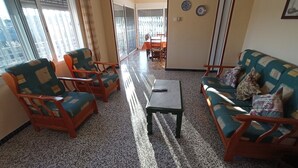 Ein Wohnzimmer mit einer Couch, zwei Sesseln, einem Couchtisch und einem Essbereich im Hintergrund.