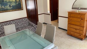 Una habitación con una mesa de vidrio, un aparador de madera, un cuadro en la pared y un piso estampado.