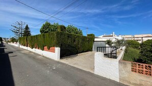 Una calle residencial con pavimento, un muro blanco con base de ladrillo y un portón de metal negro.
