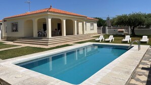 Et poolområde med pool, en overdækket patio med stole, og en bygning med et tegltag.