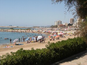 A beach with people, umbrellas, and buildings in the background.