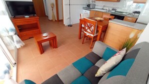 Una sala de estar con sofá, mesa de centro, televisor y una cocina con microondas y armarios.