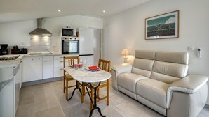 A compact kitchen with modern appliances, a dining table with chairs, and a sofa in a living area with a painting on the wall. - 1 bedroom lovely home in Saujon (Saujon)