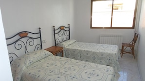 Ein Zimmer mit zwei Betten, einem kleinen Tisch, einem Stuhl und einem Fenster mit Jalousien.