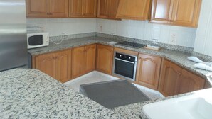 Eine Küche mit Holzschränken, einem Edelstahlkühlschrank, einer Mikrowelle, einem Backofen und Granit Arbeitsplatten.